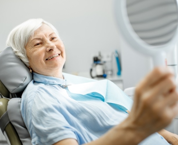 Woman looking at her new smile after dentures in the mirror
