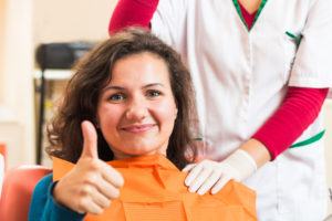 Woman smiling in dental chair giving thumbs up